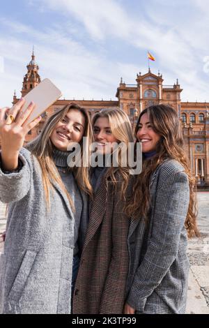 Rückansicht einer Gruppe von nicht erkennbaren Frauen in stilvollem Outfit, die am Wochenende an der Plaza de Espana an einem sonnigen Tag in Sev Selbstschuss auf dem Smartphone gemacht haben Stockfoto