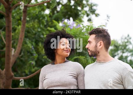 Mid-Shot-Porträt einer afroamerikanischen Frau und eines kaukasischen Mannes, der sich ansieht und eine gute Zeit im Freien hat Stockfoto