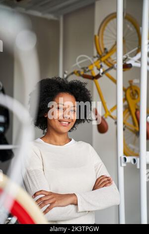 Porträt einer afroamerikanischen Unternehmerin, die in ihrem Fahrradladen posiert und von Fahrrädern umgeben ist Stockfoto