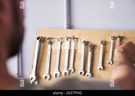 Foto eines nicht fokussieren Mannes, der einen Schraubenschlüssel aus einer Werkzeugwand nimmt Stockfoto