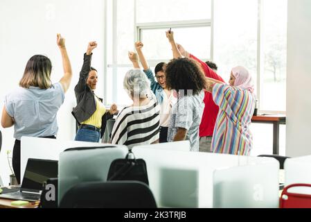 Eine Gruppe von glücklichen, vielfältigen Mitarbeitern, die mit erhobenen Armen im Kreis stehen und ein erfolgreiches Business-Projekt im Light Office in Costa Rica in da feiern Stockfoto