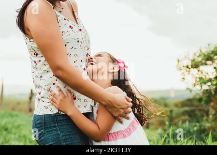 Seitenansicht einer zugeschnittenen, nicht erkennbaren glücklichen Frau auf dem Feld, die lächelt und ein kleines Mädchen anschaut, während sie am Wochenende gemeinsam auf dem Feld unterwegs ist Stockfoto