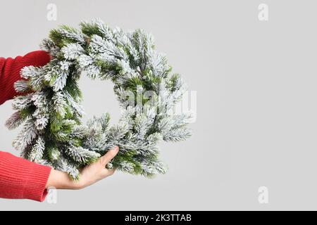 Frau in rotem Pullover mit Weihnachtskranz aus Fichtenzweig auf weißem Hintergrund. Festliche Dekoration für Weihnachten. Banner mit Kopierbereich. Stockfoto