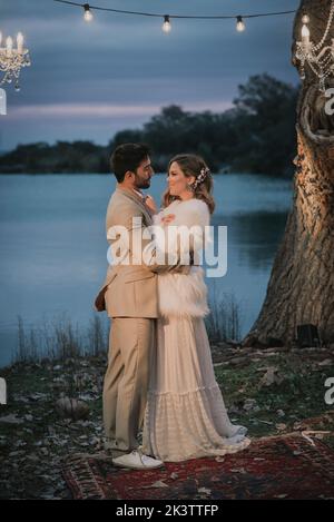 Seitenansicht des jungen Mannes in grauem Kostüm umarmt und küsst attraktive lächelnde Dame im Hochzeitskleid Stockfoto