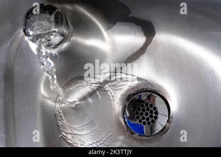 Glänzendes Waschbecken aus Stahl mit Wasser, das den Abfluss hinunterfließt Stockfoto