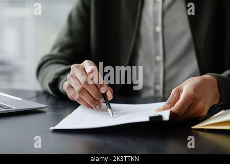 Nahaufnahme eines anonymen schwarzen Mannes, der den Vertrag bei der Besprechung liest und ihn mit einem Stift unterschreibt, Kopierbereich Stockfoto