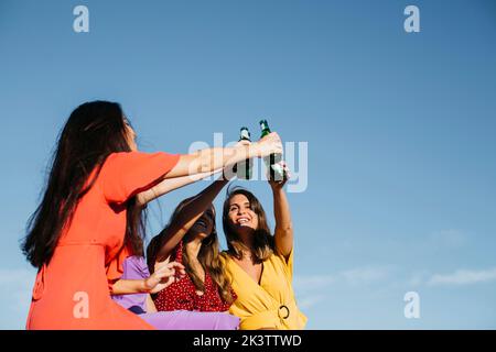 Unten der Gruppe der fröhlichen Freundinnen toasten und klirrenden Glasflaschen des Bieres Stockfoto