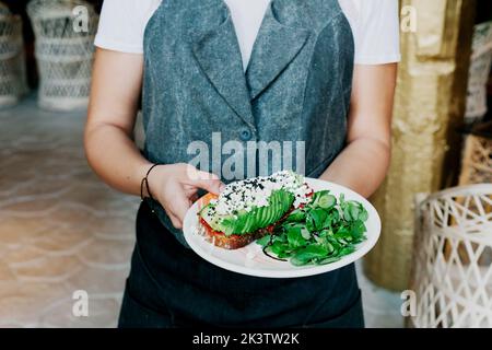 Von oben Ernte kochen Halteplatte mit leckeren großen appetitlichen Sandwich mit Avocado-Sauce und Grüns Stockfoto