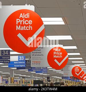 Tesco Supermarkt Interior Shopping Aisle repetitive Runde Aldi Price Match Werbeschilder hängen zwischen Beleuchtungspaneelen über Essex England UK Stockfoto