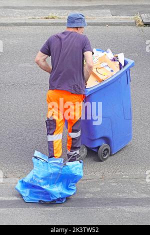 Rückansicht des Binmans, der den Inhalt des Blue council entleerte, gab einen Recycling-Sack aus Haushaltspapier aus Pappe in den Mülltonne und ließ ihn auf dem Bürgersteig in Großbritannien liegen Stockfoto