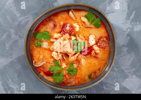 Traditionelle thailändische Küche. Tom Yum würzige Suppe in schwarzer Schüssel auf grauem Hintergrund. Thailändisches Essenskonzept. Draufsicht Stockfoto