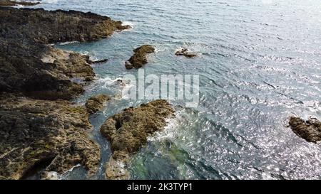 Wilde Felsküste des Atlantischen Ozeans. Kleine Wellen und Sonnenstrahlen auf der Wasseroberfläche. Küstenlandschaft an einem sonnigen Tag. Stockfoto