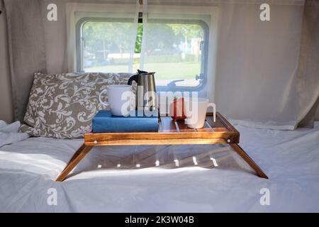 Tassen Kaffee und Geysir-Kaffeemaschine auf Holztablett für das Frühstück auf dem Bett im Wohnwagen Stockfoto
