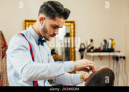 Ein Barbier schneidet in einem Friseursalon den Bart eines Mannes mit einem Rasiermesser Stockfoto
