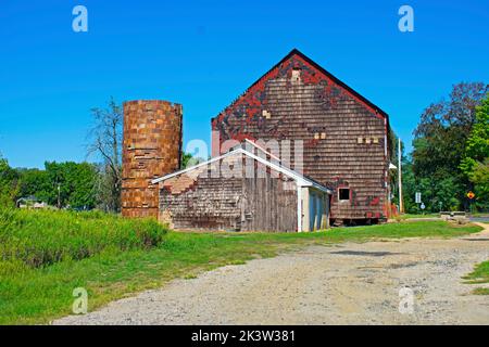 Alte rote Scheune, die dringend einer Reparatur bedarf, auf einem grasbewachsenen Feld an einem klaren und sonnigen Tag -02 Stockfoto