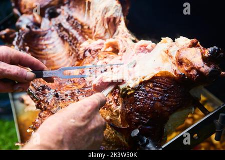 Der Koch schneidet das ganze gegrillte Schweinefleisch für Steaks mit einem Messer. Vom Schwein gegrillte traditionelle Kohle und Feuer. Das kleine Ferkel wird ganz auf einem offenen Feuer geröstet Stockfoto