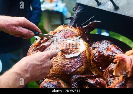 Der Koch schneidet das ganze gegrillte Schweinefleisch für Steaks mit einem Messer. Vom Schwein gegrillte traditionelle Kohle und Feuer. Das kleine Ferkel wird ganz auf einem offenen Feuer geröstet Stockfoto