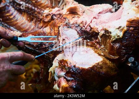 Der Koch schneidet das ganze gegrillte Schweinefleisch für Steaks mit einem Messer. Vom Schwein gegrillte traditionelle Kohle und Feuer. Das kleine Ferkel wird ganz auf einem offenen Feuer geröstet Stockfoto