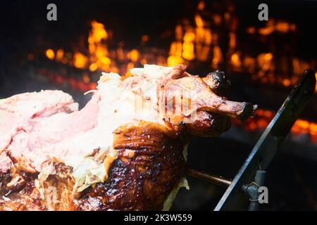 Der Koch schneidet das ganze gegrillte Schweinefleisch für Steaks mit einem Messer. Vom Schwein gegrillte traditionelle Kohle und Feuer. Das kleine Ferkel wird ganz auf einem offenen Feuer geröstet Stockfoto
