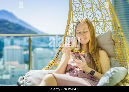 Portrait einer wunderschönen Frau in einem wunderschönen Kleid, die auf einer Terrasse sitzt und Erdbeere isst Stockfoto