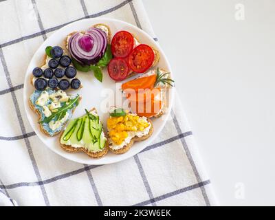 Rainbow Sandwiches in Herzform auf weißem Tisch. Frühstücksbrot Regenbogen Sandwiches mit buntem Gemüse. Liebe, Valentinstag Essen und LGBT Stolz f Stockfoto