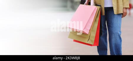 Schwarzer freitag. Banner mit verkürzten Beinen der Frau mit bunten Einkaufstaschen im Hintergrund eines städtischen Einkaufszentrums. Käufe, Rabatte, Verkaufskonzept. Online Stockfoto