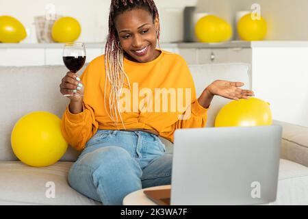Virtuelle Party. afroamerikanische Frau, die mit Freunden einen Videoanruf führt, ein Glas Wein hält und Geburtstag feiert Stockfoto