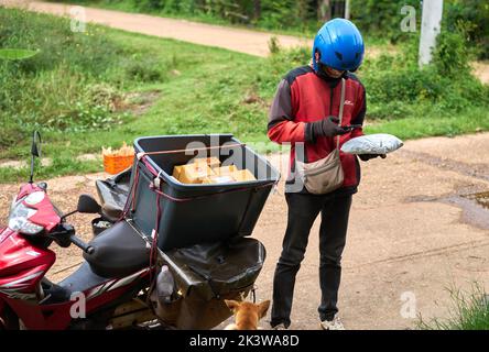 Ein Motorradkurier liefert Pakete in einem ländlichen Gebiet. Stockfoto