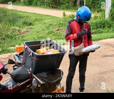 Ein Motorradkurier liefert Pakete in einem ländlichen Gebiet. Stockfoto