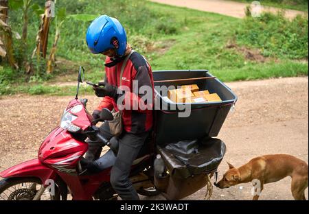 Ein Motorradkurier liefert Pakete in einem ländlichen Gebiet. Stockfoto