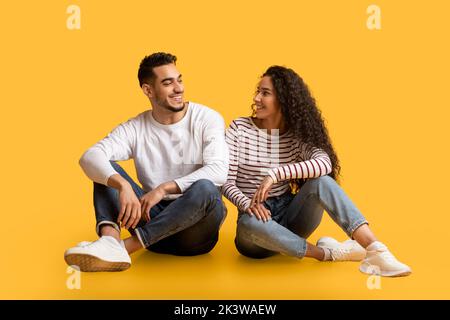 Porträt eines schönen jungen nahöstlichen Paares, das auf gelbem Hintergrund sitzt Stockfoto