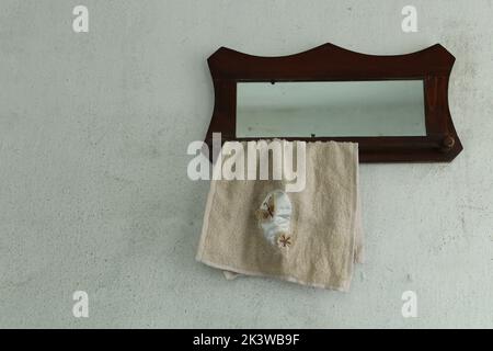 Alte hölzerne Kleiderbügel für Handtücher mit Spiegel an der alten Wand. Stockfoto