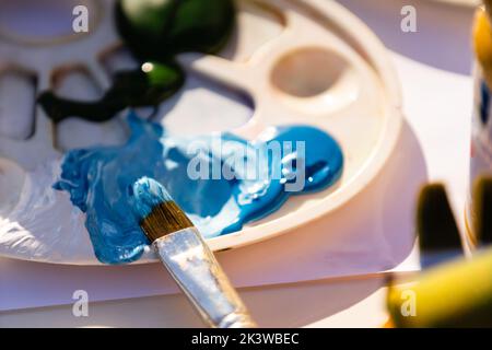 Farben und Pinsel im Prozess der Arbeit, Palette mit gemischten Farben. Stockfoto