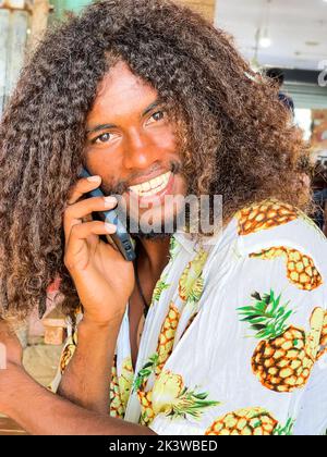 Fröhlich lächelnd Singhalesisch junger Mann Porträt ruft jemand mit einem Smartphone. Natürliche Menschen oder Kommunikationstechnik Konzept. Stockfoto