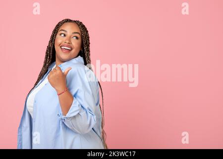 Schwarzes Weibchen Zeigt Den Daumen Zur Seite Auf Den Kopierbereich, Rosa Hintergrund Stockfoto