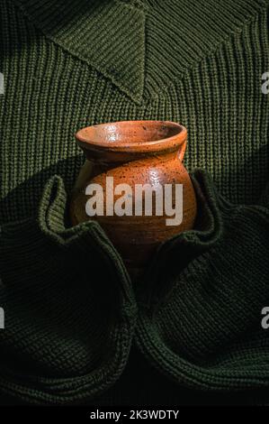 Vertikales Bild eines gestrickten Army Green Pullovers mit einer Keramikschale Stockfoto