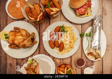 Verschiedene Fast-Food-Gerichte mit Kroketten, gegrilltem Hähnchen, Kartons mit Kartoffeln und gebratenen Hähnchenstreifen, Lamm-Kebab-Sandwich und Durum mit Halal-Fleisch Stockfoto