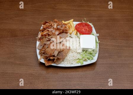 Typischer Kombi-Teller pakistanischer Restaurants in europa mit Lamm- und Hühnchen-Kebab-Brötchen mit pommes Frites, weißem Reis, Feta-Käse und Salat Stockfoto