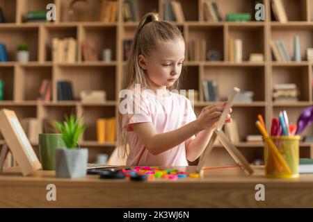 Kleines Mädchen, das mit Brett am Tisch sitzt, Wörter aus bunten Buchstaben macht, bei Kinderentwicklungskursen trainiert Stockfoto