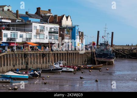 Der kommerzielle Fischereihafen in Bridlington East Yorkshire, mit kleinen und größeren Fischerbooten entlang der Hafenmauer und Geschäften am Kai. Stockfoto