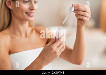Beauty- und Hautpflegekonzept. Frau mittleren Alters, die die Flasche mit feuchtigkeitsspendendem Gesichtsserum hält und öffnet, abgeschnitten Stockfoto