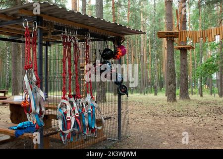 Kinderseilpark in einem Kiefernwald. An Karabinern hängen Sicherheitsseile. Schutzhelme hängen an einem Gitter. Gewährleistung der Sicherheit von Aktivitäten für Kinder Stockfoto