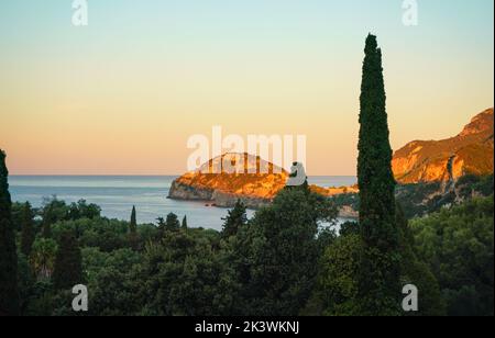 Die Morgensonne scheint über den Hügeln in der Nähe der Liapades Bucht in Korfu, hohe Bäume im Vordergrund. Sonnenaufgang an der Küste Stockfoto