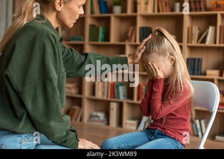 Kleine verängstigte Mädchen versteckt Gesicht hinter den Händen, ignoriert fürsorgliche weibliche Psychologin während der persönlichen Beratung im Büro Stockfoto