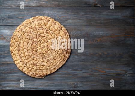 Weidenstroh legen Matte auf Holz dunklen Hintergrund. Runde gewebte Strohmatte auf grauem Holztisch. Menü, Essen, Essen Konzept. Draufsicht, Kopierer-SPAC Stockfoto