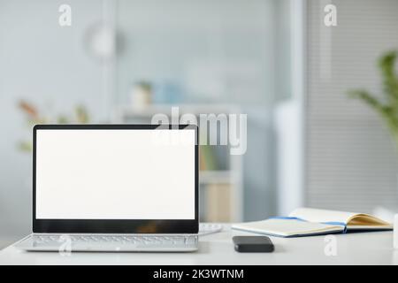 Minimales Hintergrundbild eines geöffneten Laptops mit weißem Bildschirm-Mockup am Arbeitsplatz im Büroinneren in Weiß- und Grautönen, Kopierbereich Stockfoto