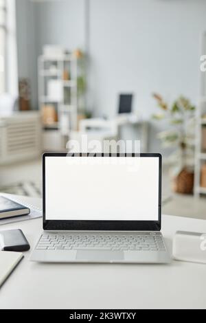 Vertikales Hintergrundbild eines offenen Laptops mit weißem Bildschirm in minimalem Weiß- und Grauton am Arbeitsplatz Stockfoto