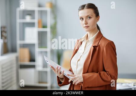 Porträt einer jungen erfolgreichen Geschäftsfrau, die im Büro die Kamera anschaut und Dokument und Kopieplatz hält Stockfoto