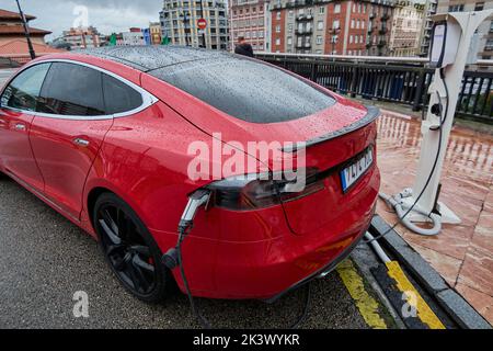 Rotes Elektroauto, das an einem regnerischen Tag auf der Straße geladen wird. Konzept der Elektrifizierung von Fahrzeugen für eine bessere Umwelt durch keine CO2 emissi Stockfoto