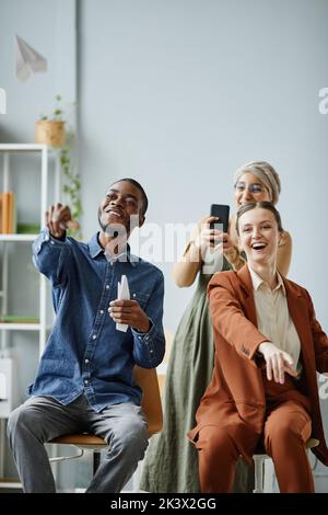 Vertikales Porträt eines jungen, vielfältigen Teams, das Spaß im Büro hat und Videos für soziale Medien filmt Stockfoto